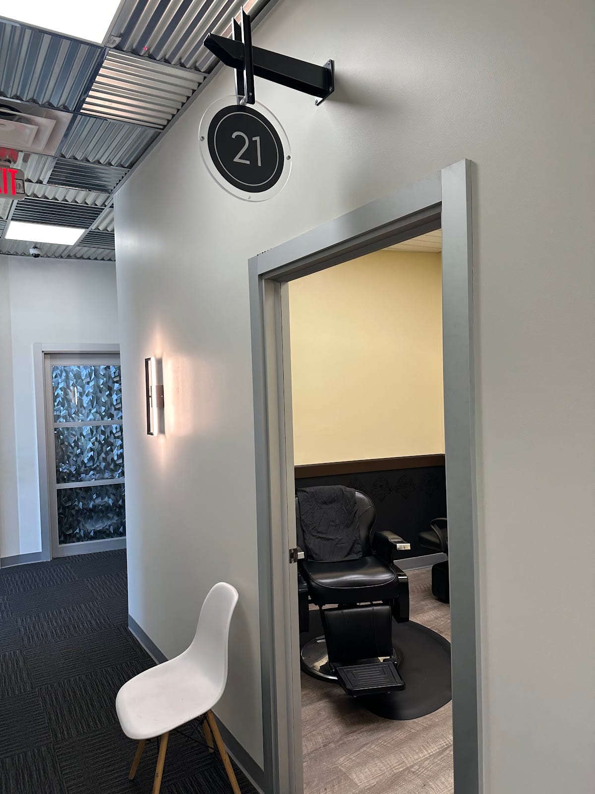 A hallway inside Sola Salons with a round black 21 sign over an open door and a barber chair inside
